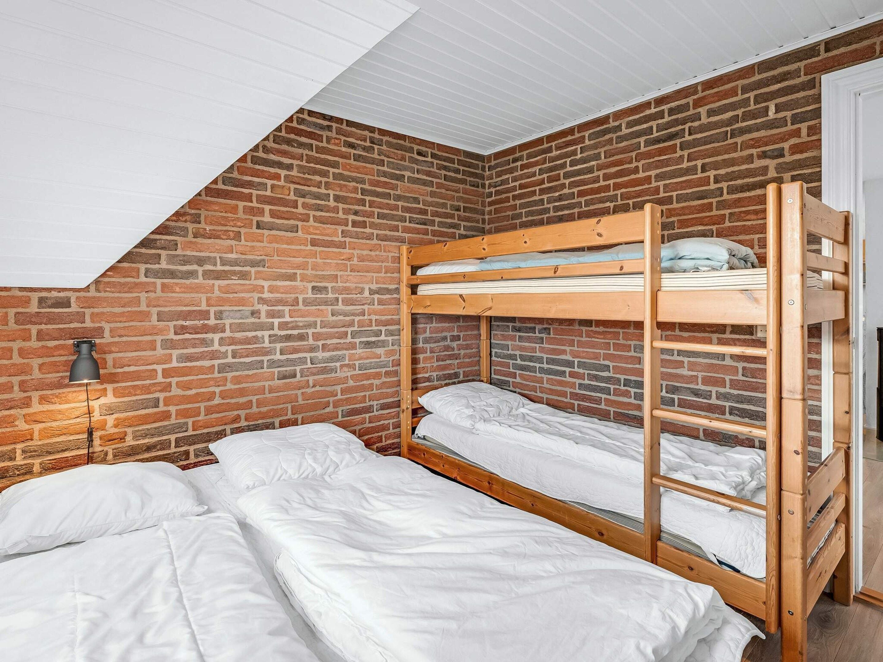 Et sovesalsværelse med murstensvæg, skråvæg og køjeseng.