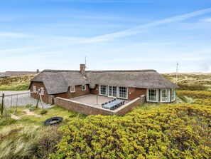 A thatched-roof house with a brick extension, a patio, and a view of the surrounding landscape. - 5 Star Holiday Home in Ringkobing (Ringkobing)
