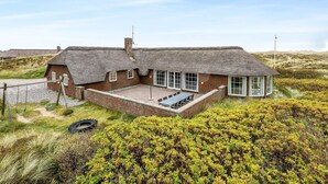 A thatched-roof house with a brick extension, a patio with outdoor seating, and a view of the surrounding landscape.