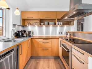A modern kitchen with wooden cabinets, stainless steel appliances, and a dishwasher. - 5 Star Holiday Home in Ringkobing (Ringkobing)