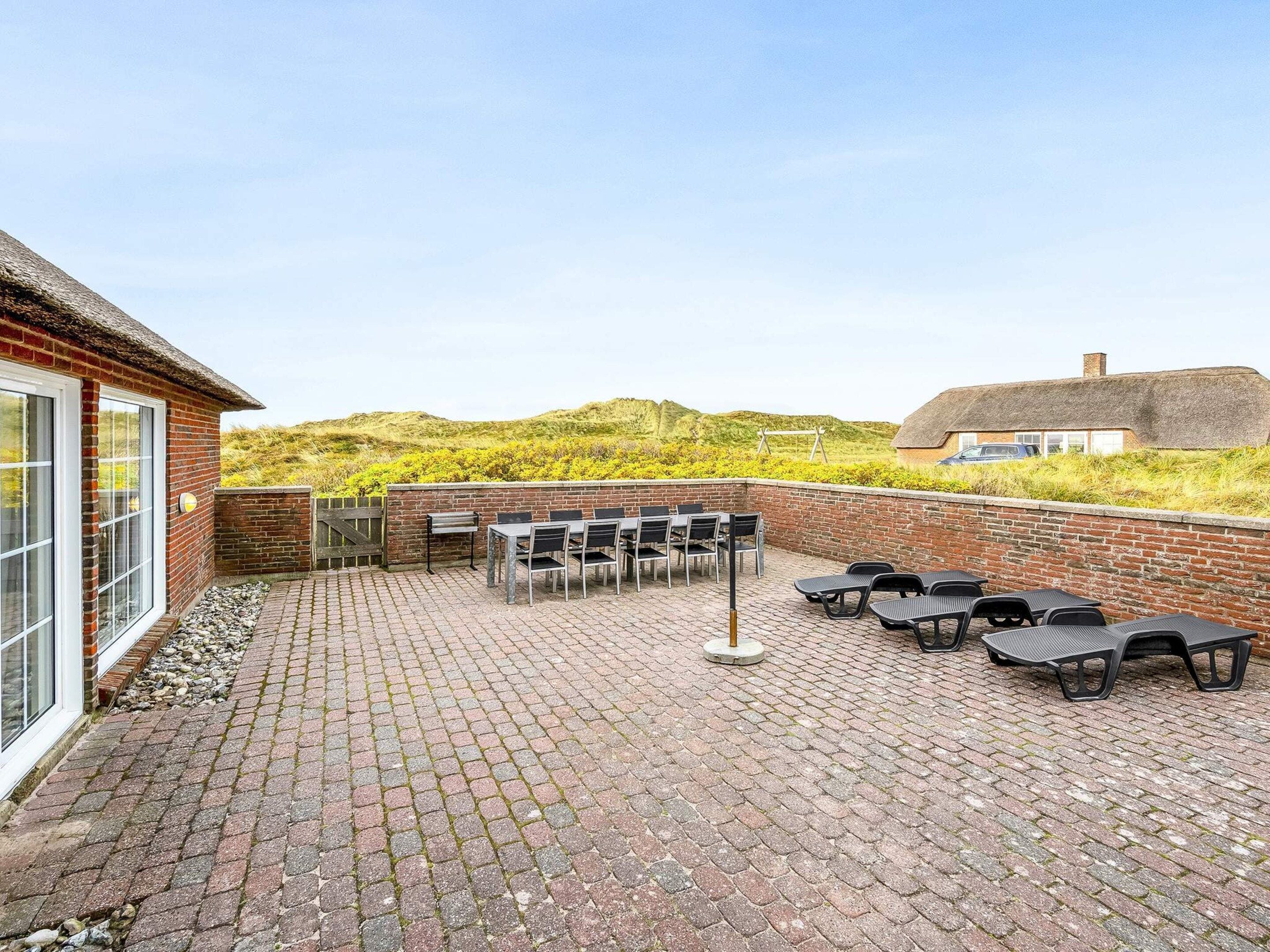 A patio with brick flooring, outdoor seating, and a view of a thatched-roof building.