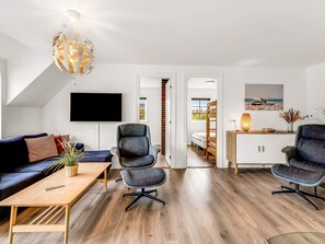 A modern living room with a wooden floor, a dark blue sofa, a grey armchair, a wooden coffee table, and a unique spherical chandelier. - 5 Star Holiday Home in Ringkobing (Ringkobing)