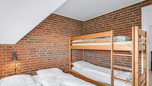 A dormitory-style room with a brick wall, a sloped ceiling, and a bunk bed.