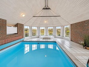 A swimming pool with a view of the outdoors, a brick wall, and a white ceiling. - 5 Star Holiday Home in Ringkobing (Ringkobing)