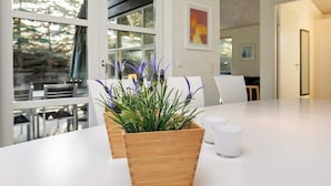 A modern kitchen with a wooden planter on the counter, a dining area with white chairs, and large windows offering a view of trees. - 8 Person Holiday Home in Hals-by Traum (Hals)