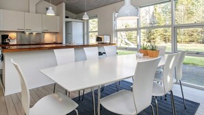 A modern kitchen with white cabinets, a wooden countertop, and a dining area with a white table and chairs. - 8 Person Holiday Home in Hals-by Traum (Hals)