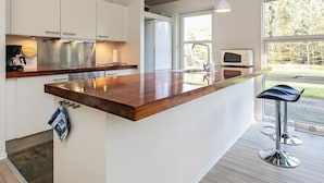 A modern kitchen with white cabinets, stainless steel appliances, and a wooden countertop. There are pendant lights, a large window, and a view of the outdoors. - 8 Person Holiday Home in Hals-by Traum (Hals)