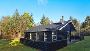 A black wooden cabin with a sloped roof and a chimney, surrounded by a grassy area and trees. - 8 Person Holiday Home in Hals-by Traum (Hals)