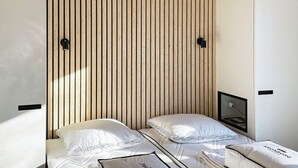 A hotel room with two beds, each with white bedding and a pillow with 'Kronborg' branding. The room has a wooden slat headboard and a small bedside table with a lamp.
