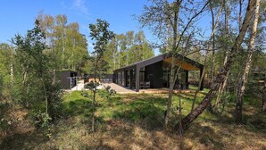 A modern cabin with a deck and outdoor seating, surrounded by trees.