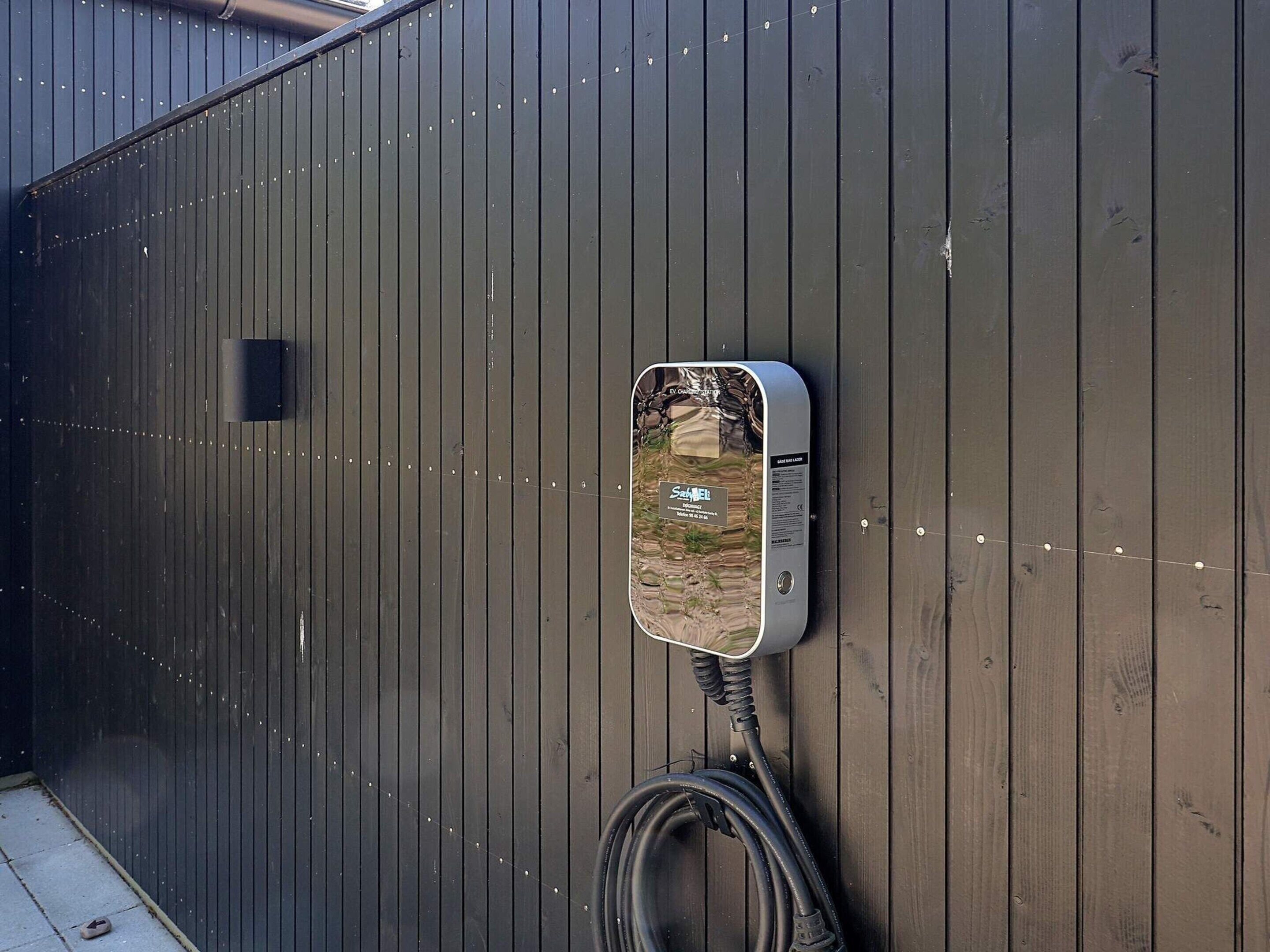 Um aquecedor de água fixado na parede, com uma mangueira conectada, em frente a uma parede de madeira escura.