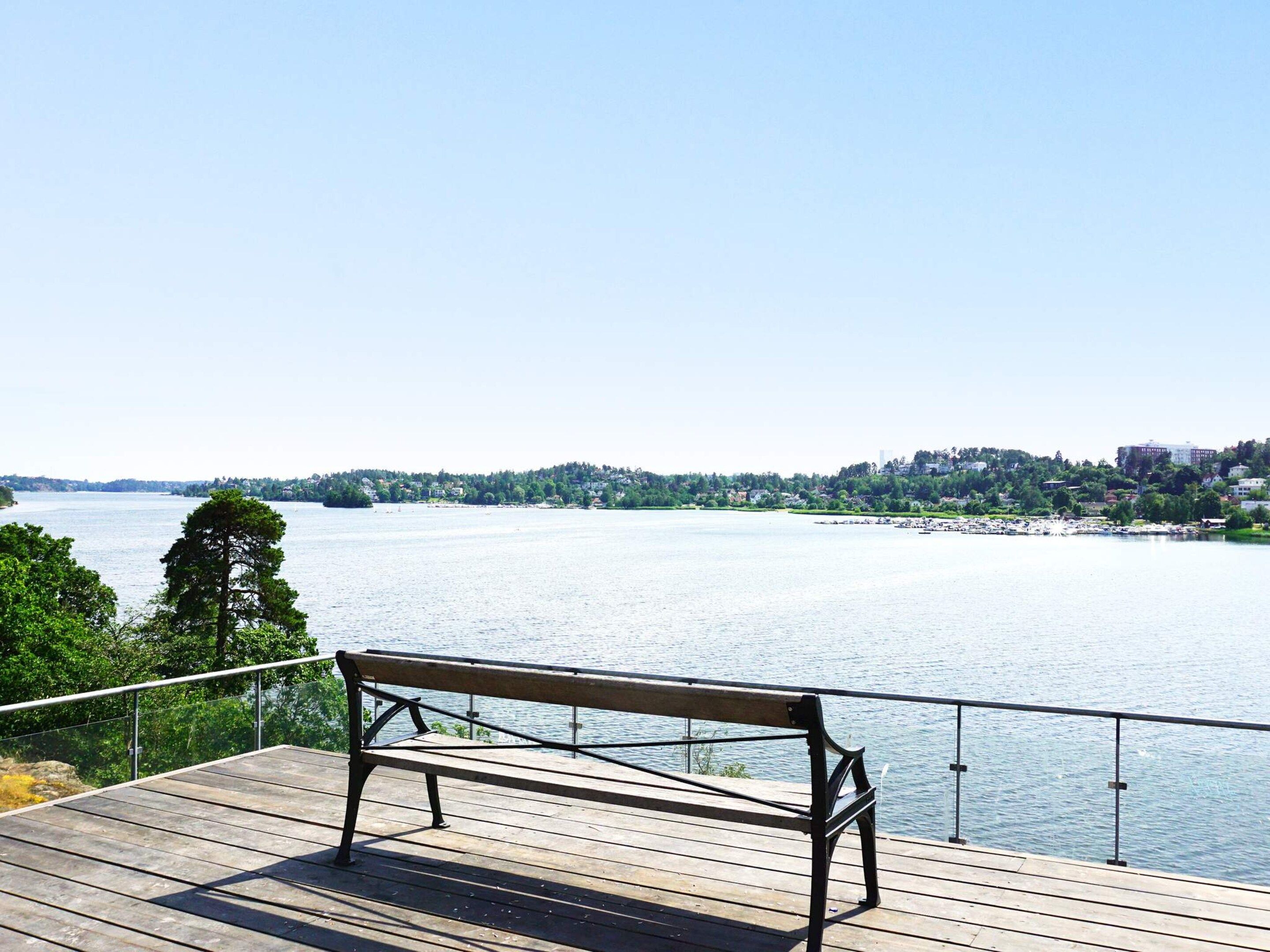 A wooden bench on a pier overlooking a calm body of water with a distant shoreline.