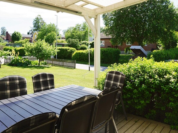 An outdoor patio with a table and chairs, surrounded by greenery and a wooden deck.