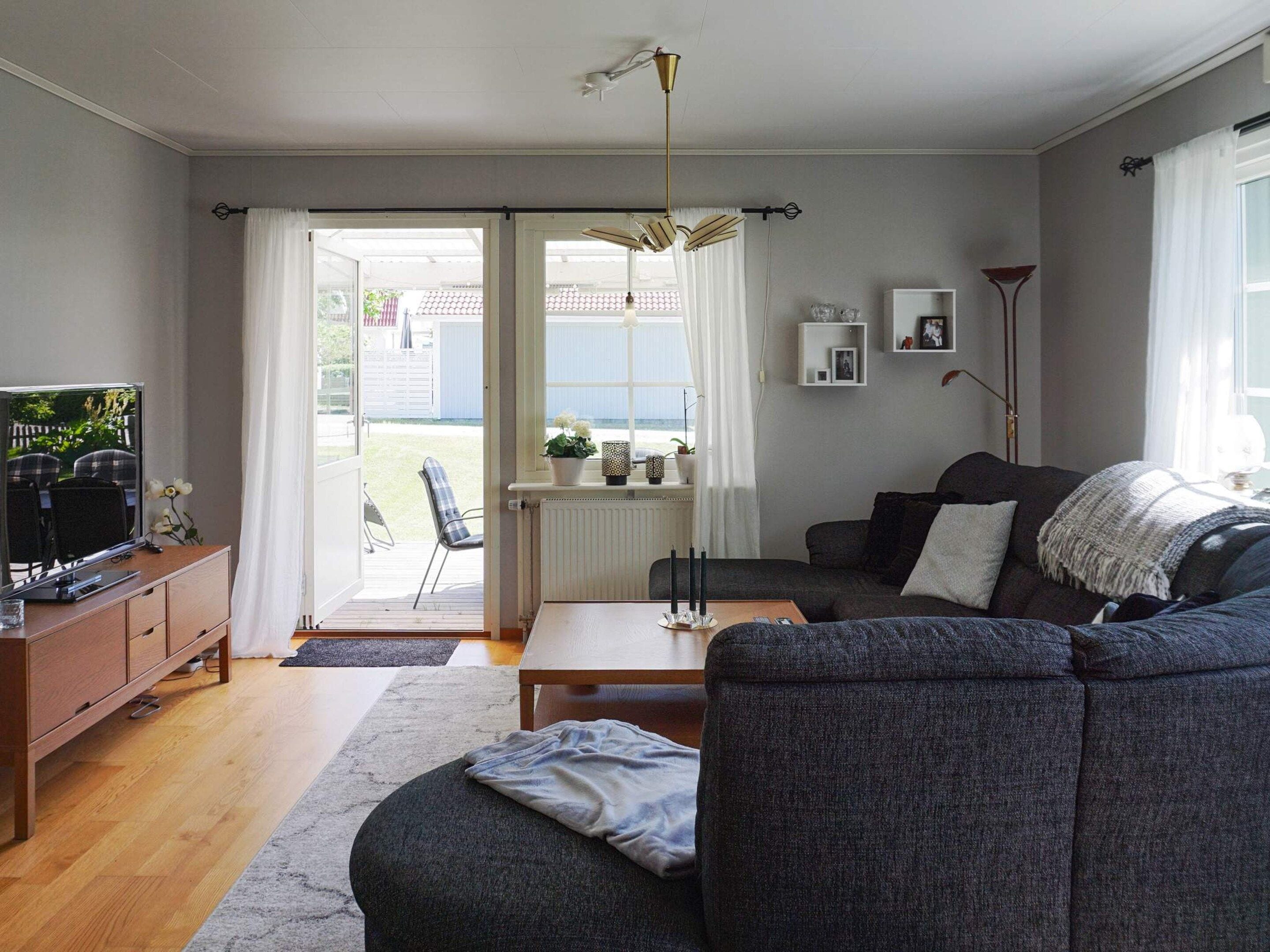 A living room with a sofa, a coffee table, a TV on a cabinet, and a view through a door to an outdoor area.