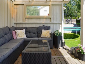A covered patio with a sectional sofa, a glass-top coffee table, and potted plants.