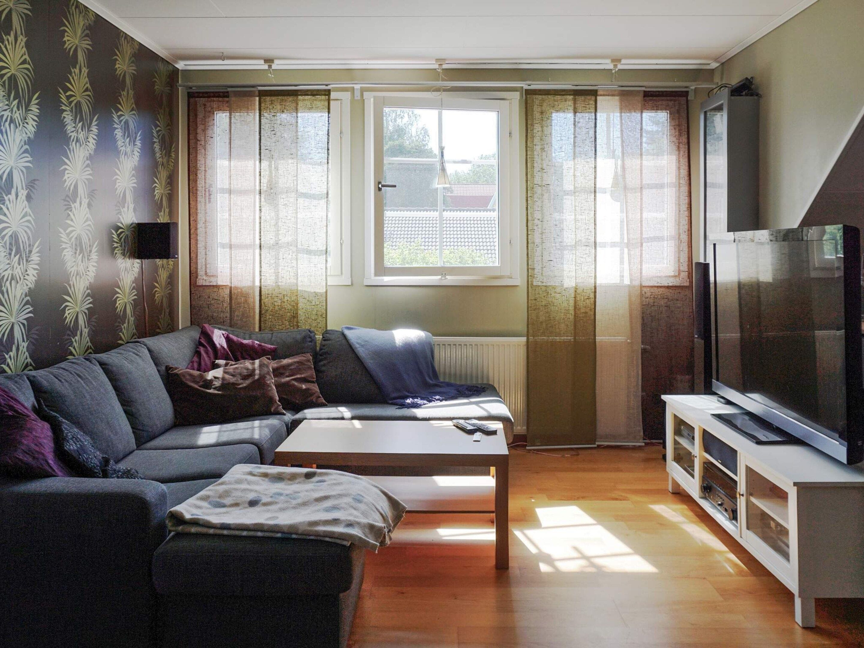 Ett vardagsrum med en soffa, ett soffbord, en tv och ett fönster med gardiner.