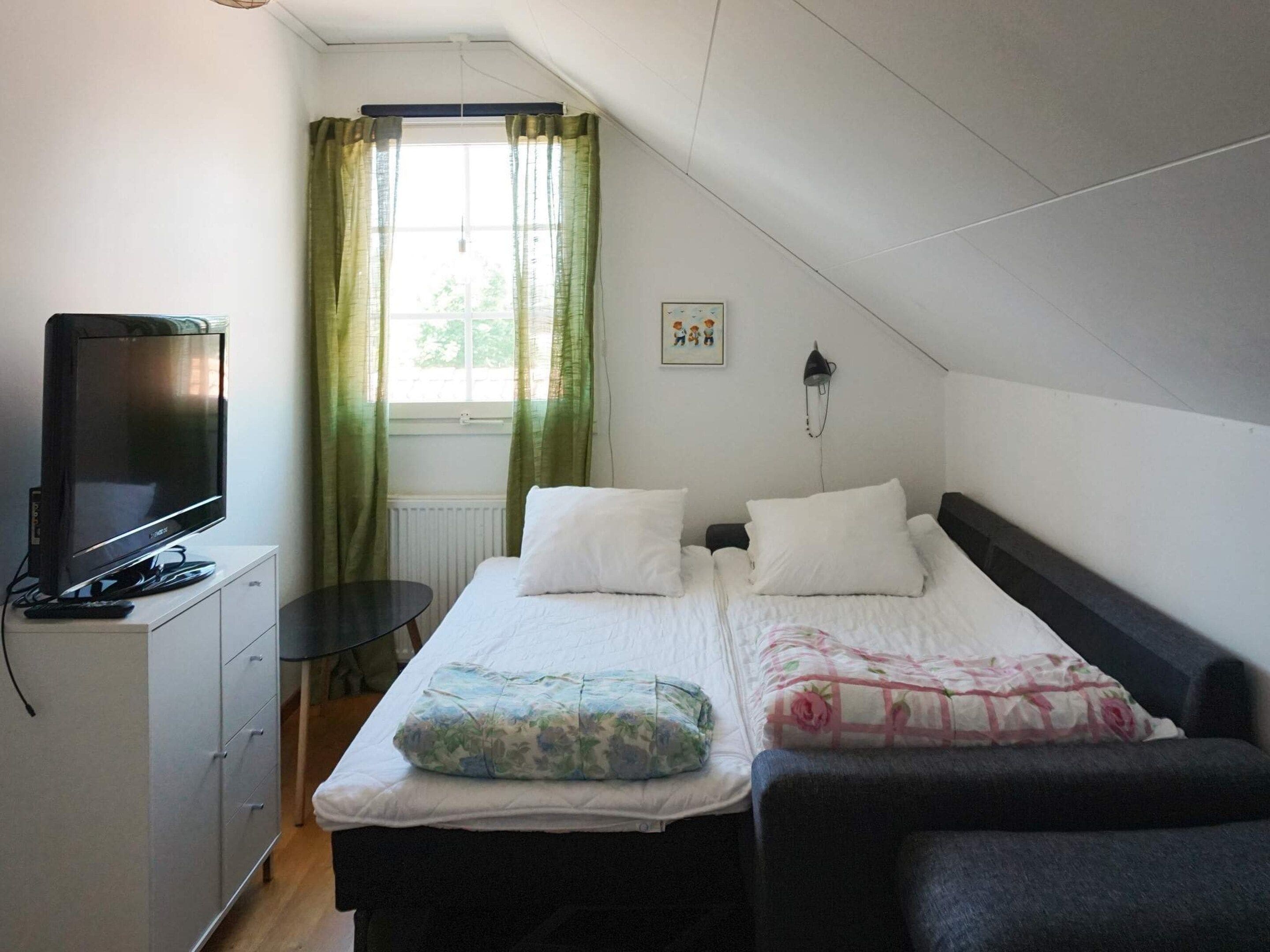 Ett sovrum med en säng, en tv, ett skrivbord och ett fönster med gardiner.