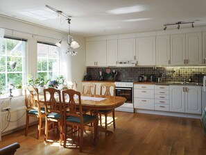 A kitchen with wooden cabinets, a dining table with chairs, and a window with plants. - 4 Star Holiday Home in Sollentuna (Sollentuna)