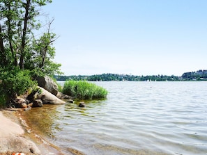 A calm lake with clear water, surrounded by trees and rocks, and a distant shoreline with buildings. - 4 Star Holiday Home in Sollentuna (Sollentuna)