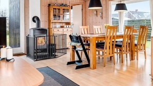 Una habitación acogedora con detalles de madera, una mesa de comedor con sillas, una parrilla negra y un armario con puertas de cristal.