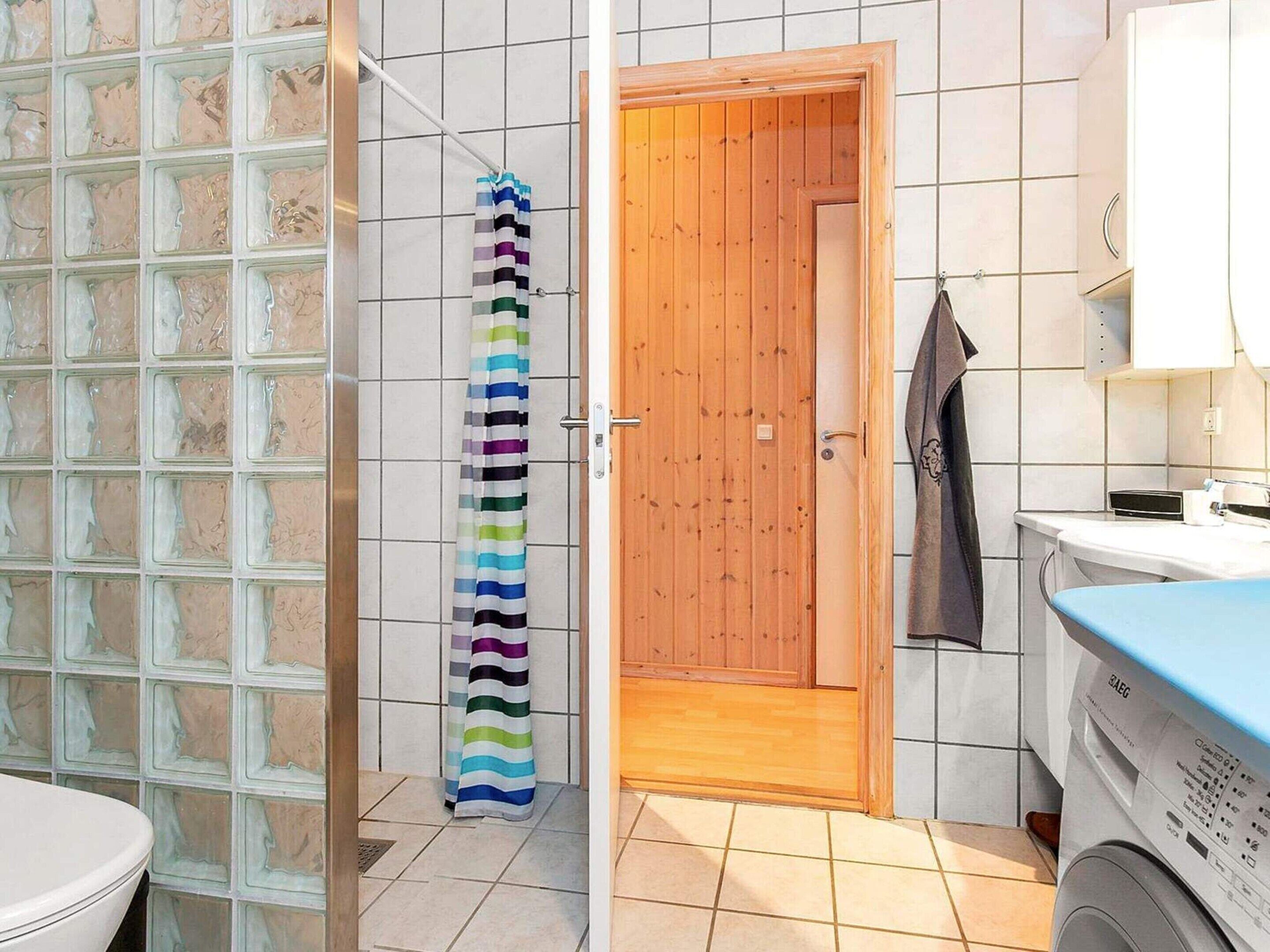 A bathroom with a shower, a wooden door, a tiled wall, a towel rack, and a washing machine.