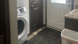 A laundry room with a washing machine, a dryer, and a door with a window. - Tiny’s  Retirement Home near the trails (Montreal)