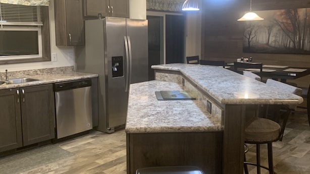A modern kitchen with granite countertops, stainless steel appliances, and a bar area with stools. - Tiny’s  Retirement Home near the trails (Montreal)