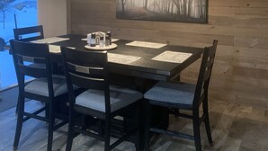 A dining area with a wooden table and chairs, a pendant light, and a painting on the wall. - Tiny’s  Retirement Home near the trails (Montreal)