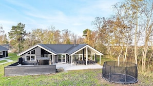 A modern house with a large patio, a covered outdoor seating area, and a trampoline in the yard. - 5 Star Holiday Home in Vaeggerlose (Vaeggerlose)