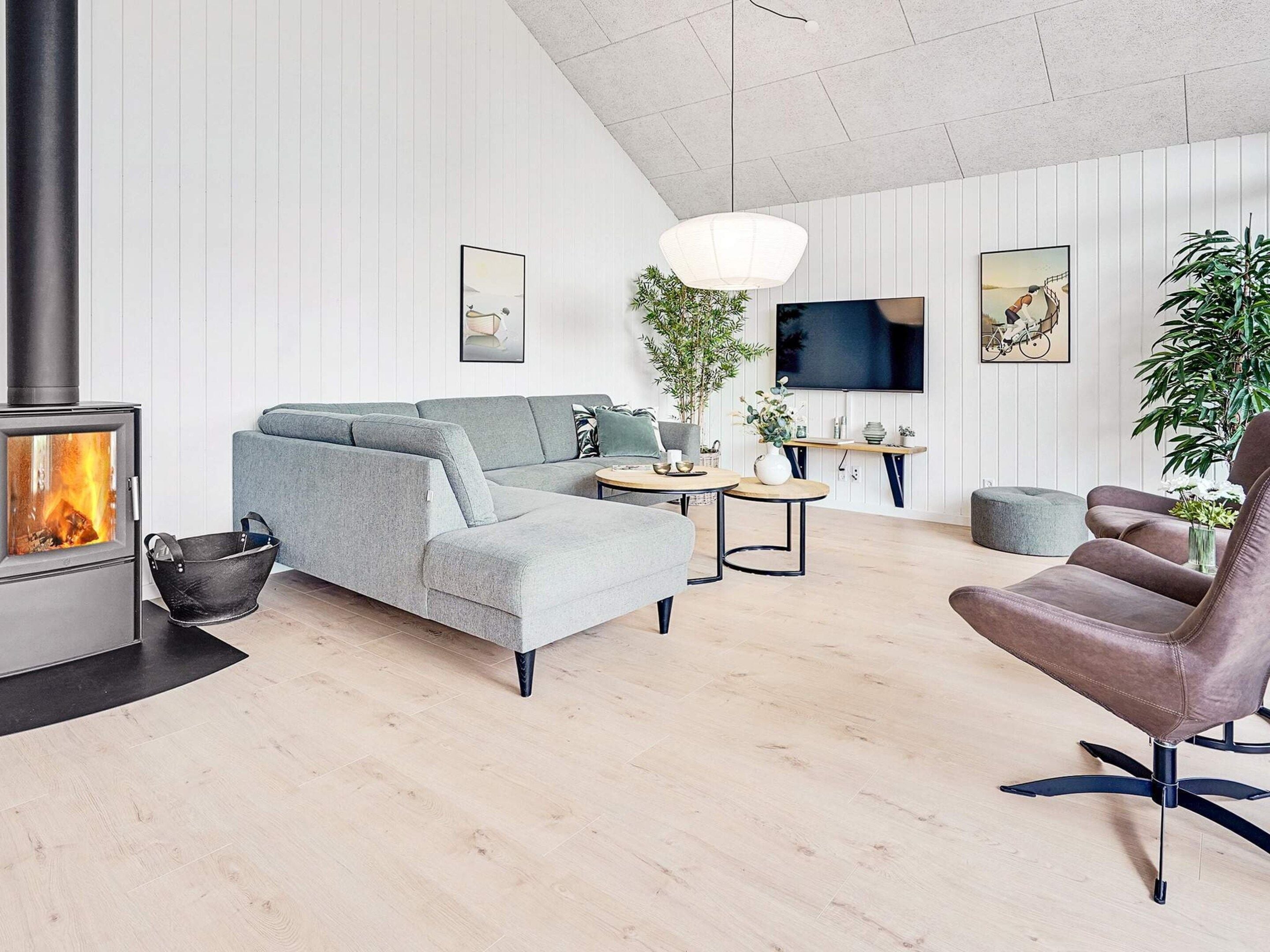 Een moderne woonkamer met een bank, een fauteuil, een televisie, een open haard en een hanglamp.