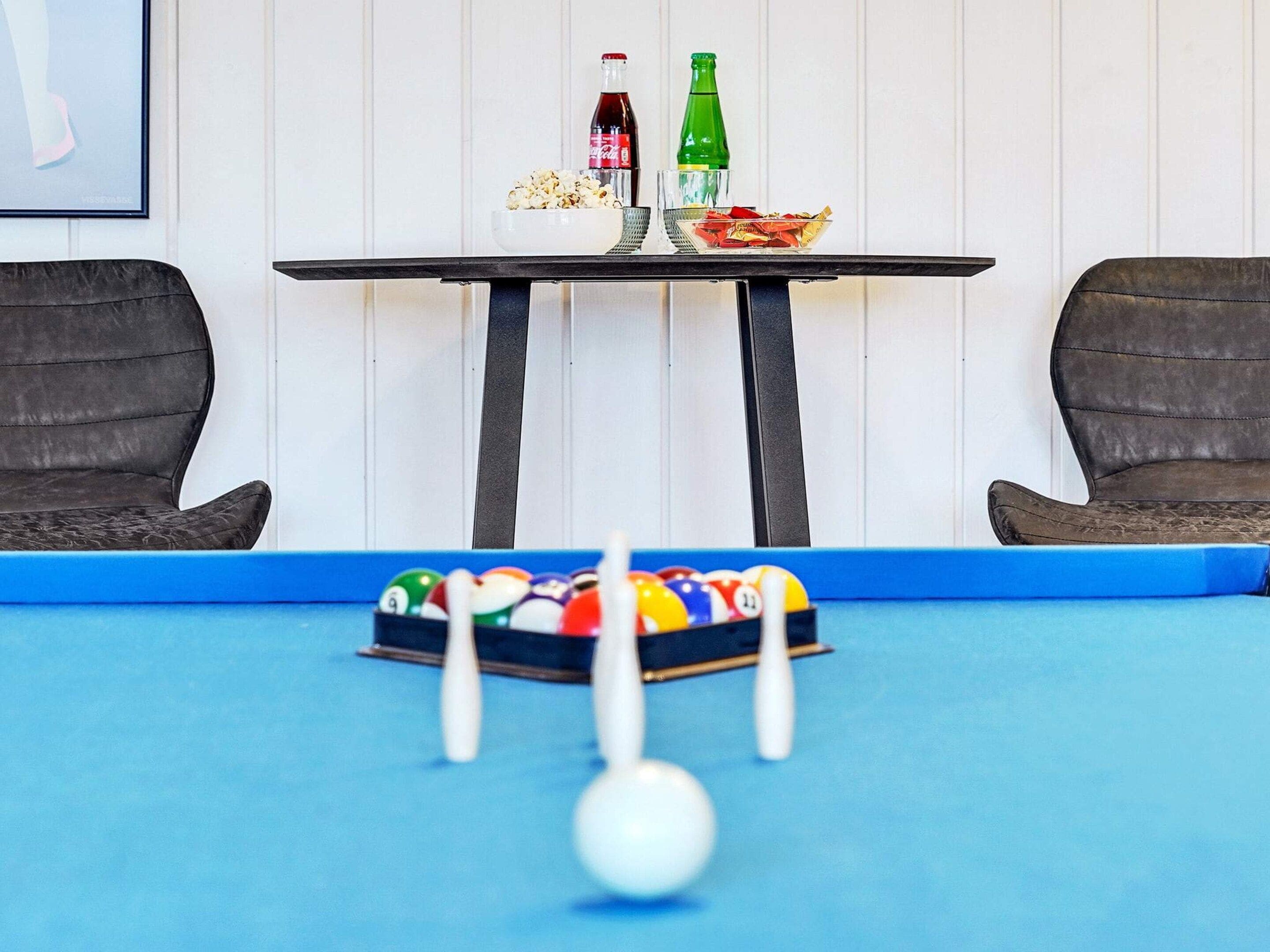 Una mesa de billar con bolas de billar, una botella de Coca-Cola, una botella de cerveza y un cuenco de palomitas de maíz.