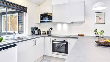 A modern kitchen with white cabinetry, a built-in oven, and a coffee machine.
