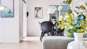 A modern living room with a grey sofa, black chairs, a dining table, and a white vase with flowers.
