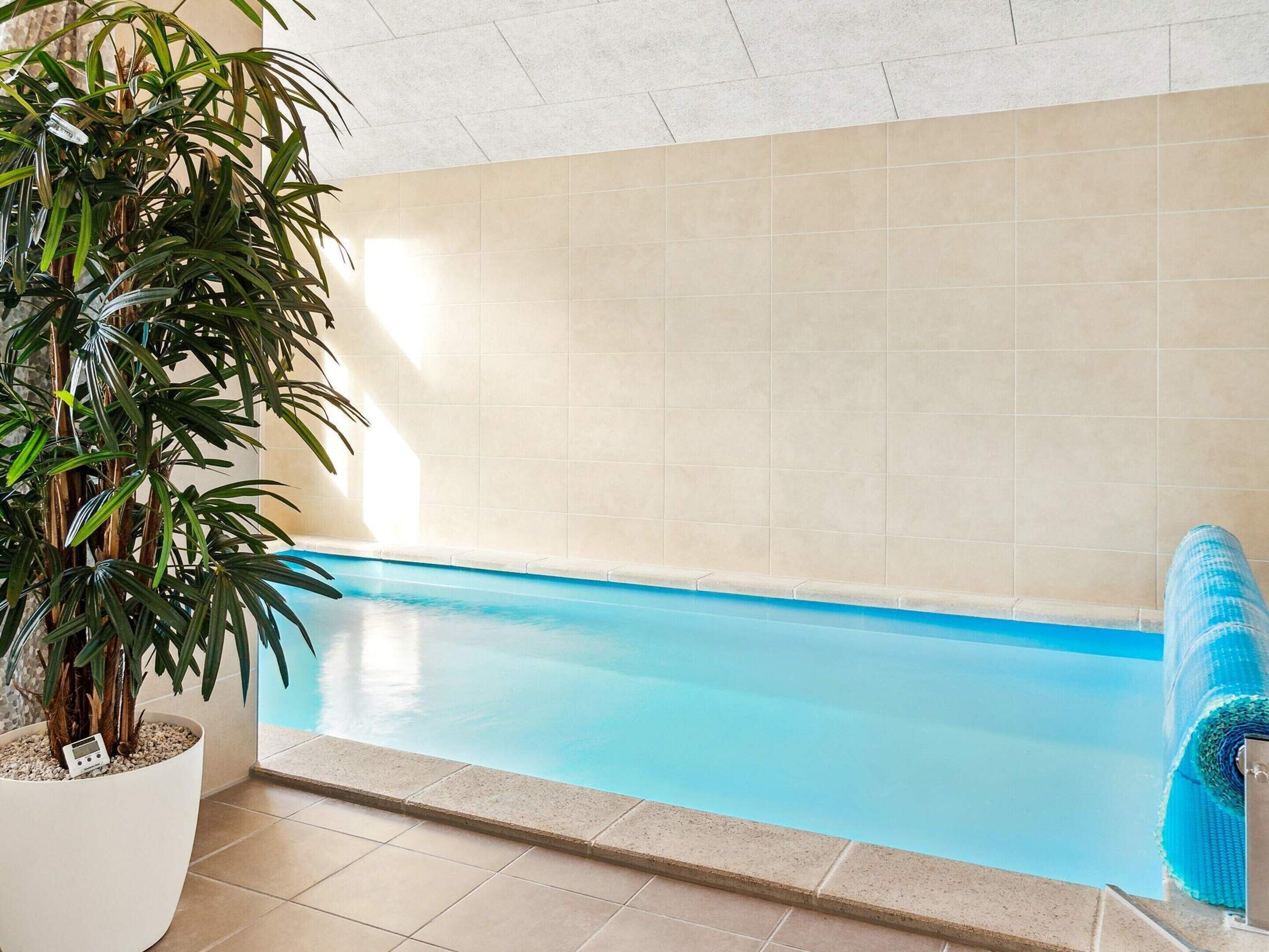 An indoor swimming pool with a tiled wall and a potted plant.