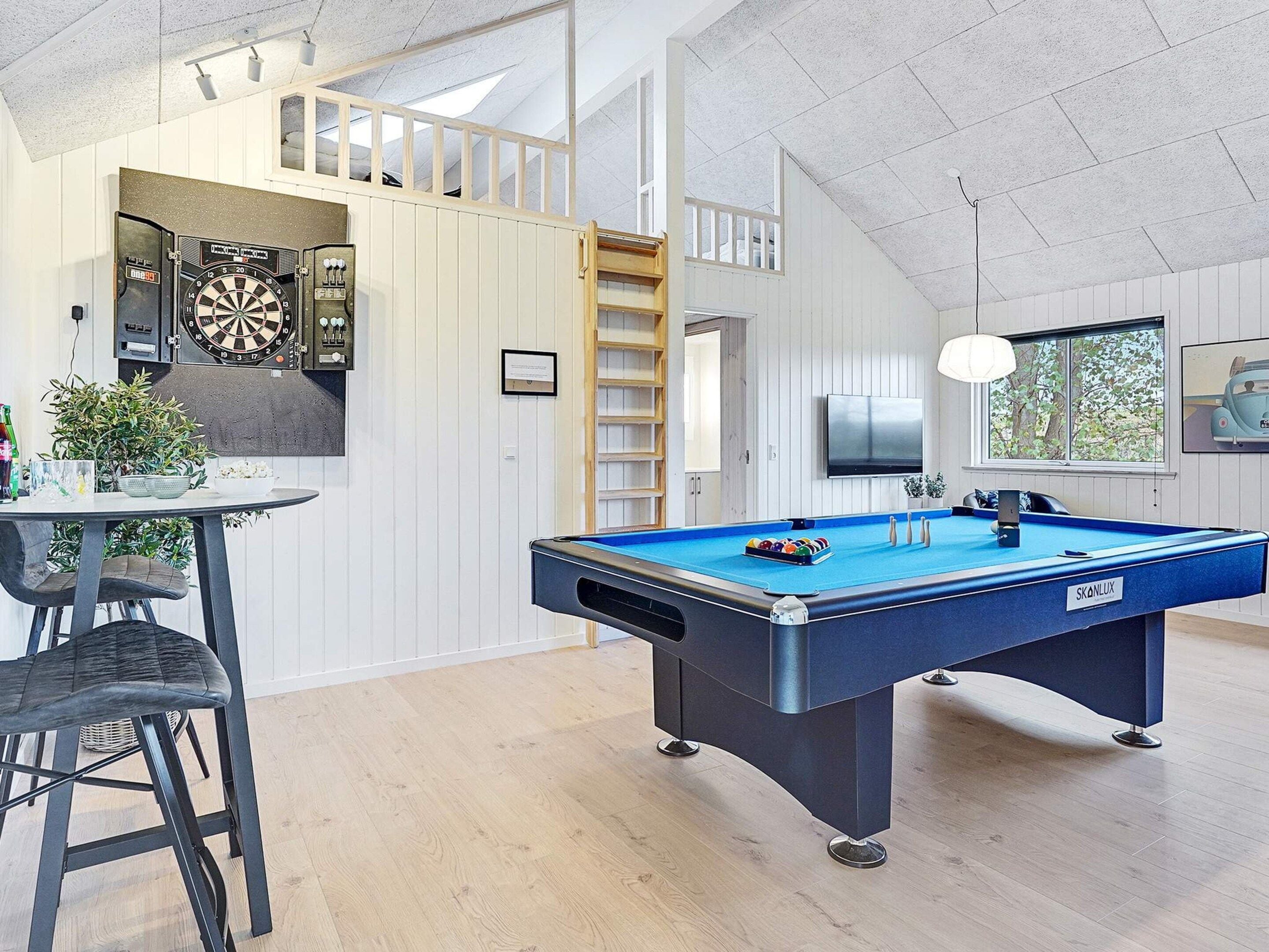 A room with a pool table, dartboard, and a television.