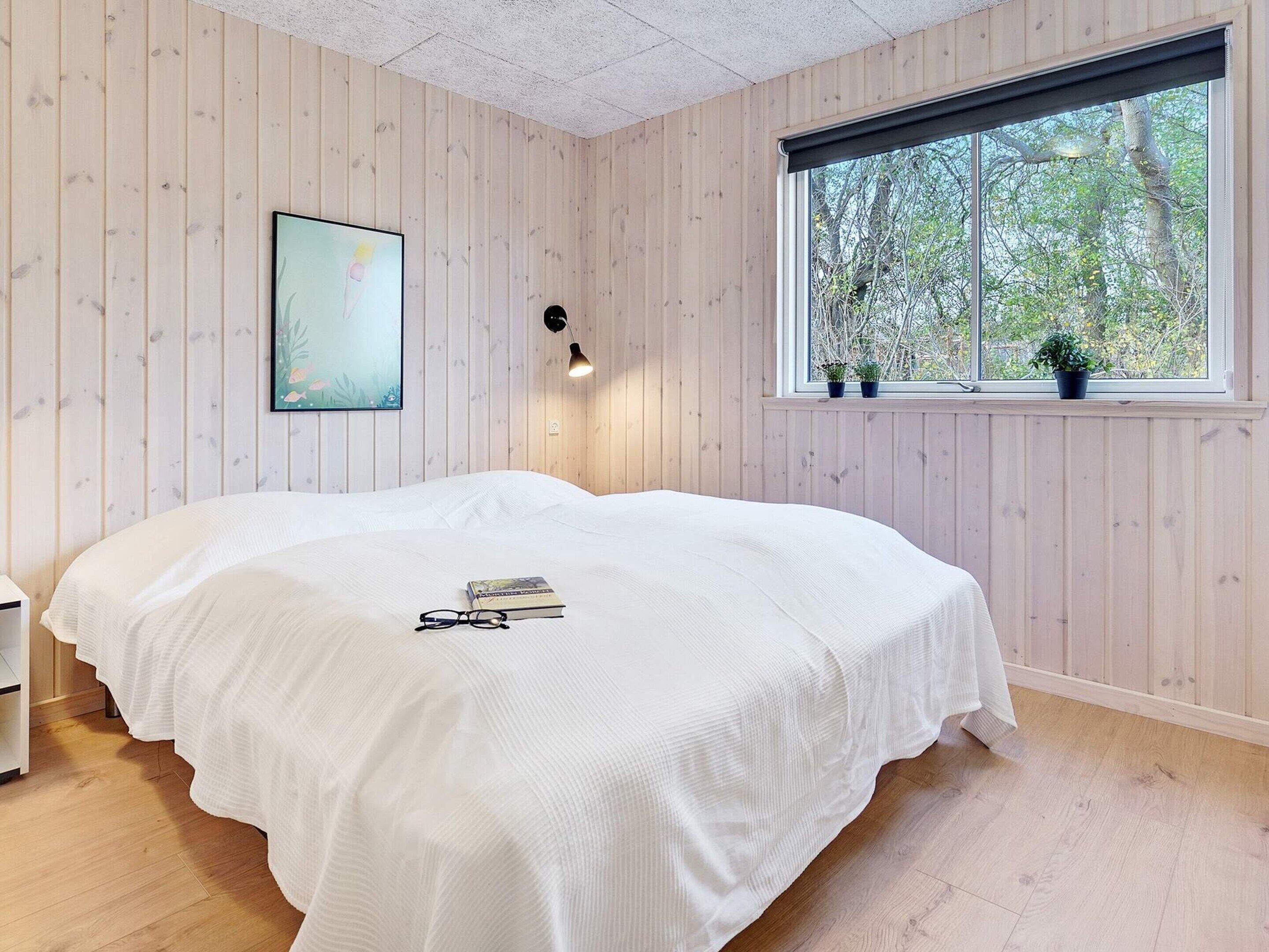Une chambre à coucher avec un lit, une fenêtre ornée de plantes, un tableau et un luminaire fixé au mur.