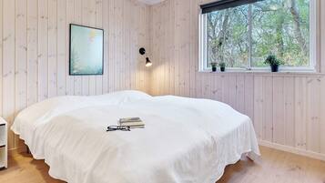 Une chambre à coucher avec un lit, une fenêtre ornée de plantes, un tableau et un luminaire fixé au mur.