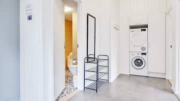 Un'area lavanderia con lavatrice, stendibiancheria in metallo e un bagno parzialmente visibile tramite una porta aperta.
