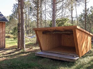 Une structure en bois, dotée d’un toit incliné, entourée d’arbres et d’herbe.