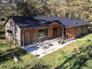 A wooden cabin with a patio, large windows, and a covered outdoor seating area.