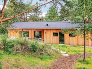 A wooden cabin with a dark roof, surrounded by trees and a grassy area.