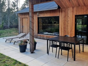 A wooden cabin with a patio area featuring a table and chairs, a lounge chair, and potted plants. - 5 Star Holiday Home in Albaek (Aalbaek)