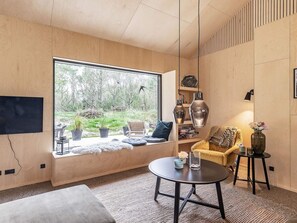 A modern living room with a large window, a sofa, a coffee table, and a bookshelf.