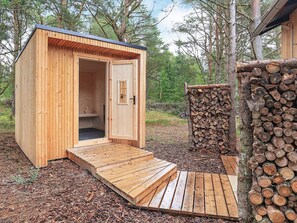 A wooden cabin with an open door, a small bench inside, and a stack of firewood outside. - 5 Star Holiday Home in Albaek (Aalbaek)