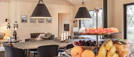 A dining area with a fruit and bread display, a table, chairs, and hanging pendant lights.