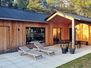 A wooden cabin with a covered patio, two lounge chairs, a table, and potted plants. - 5 Star Holiday Home in Albaek (Aalbaek)