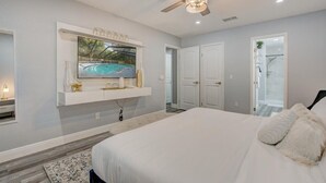 A bedroom with a large bed, a ceiling fan, a mounted TV, and a door leading to a bathroom.