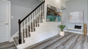 A staircase with white railings and a black handrail, a potted plant, a bench, and a framed picture on the wall.
