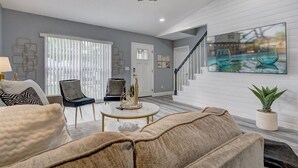A modern living room with a large window, a staircase, and a pool view.