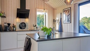 Et moderne køkken med trævægge, en stor ø, hængende lamper og et vindue med udsigt til grøn natur.
